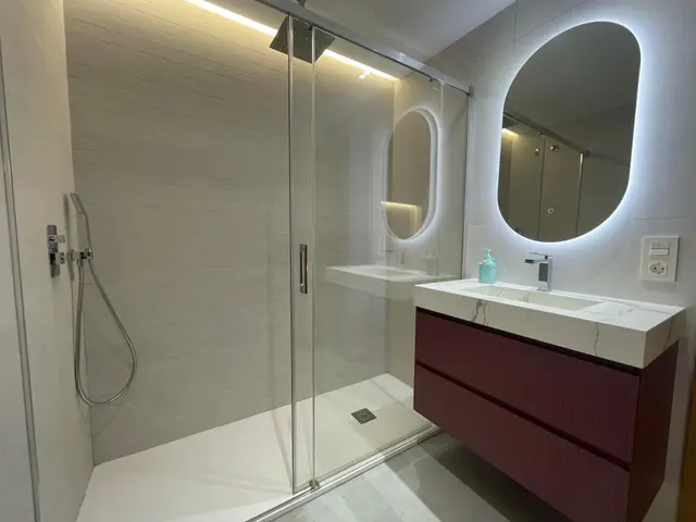 Baño con mueble suspendido granate y espejo retroiluminado, trabajo de Dos Ambients