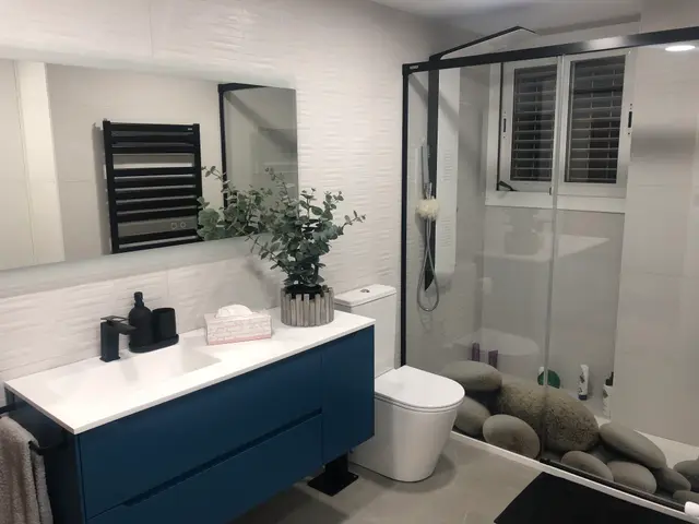 Baño con mueble azul, mampara negra y radiador toallero, trabajo de Dos Ambients