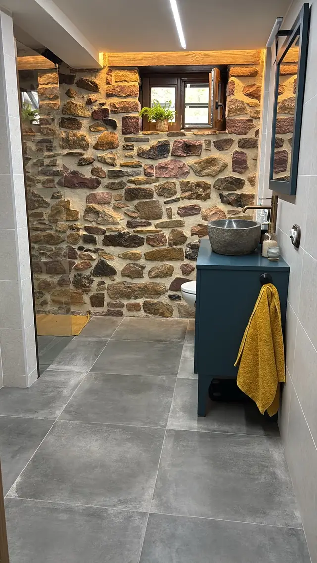 Baño rústico con pared de piedra y mueble azul, trabajo de Dos Ambients