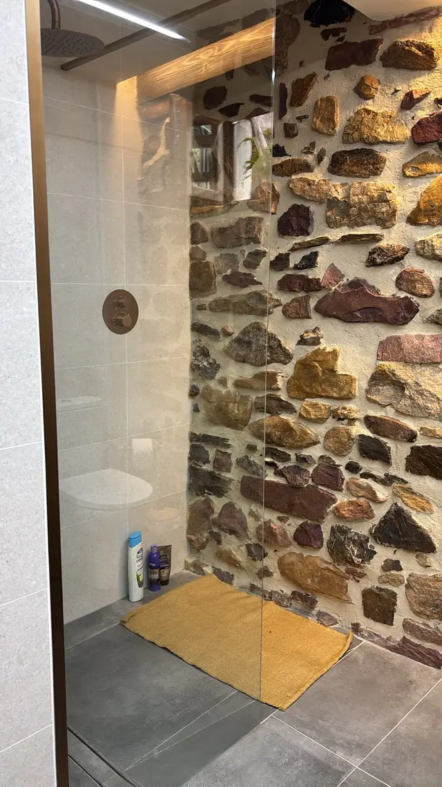 Ducha a ras de suelo con pared de piedra, trabajo de Dos Ambients