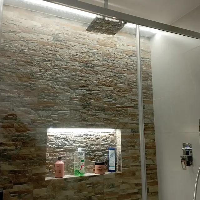 Ducha con pared de piedra y hornacina iluminada, trabajo de Dos Ambients