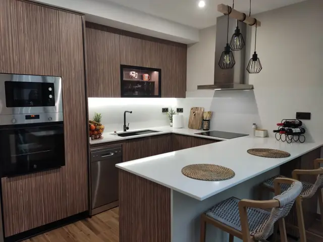 Cocina en madera con península y encimera blanca, trabajo de Dos Ambients